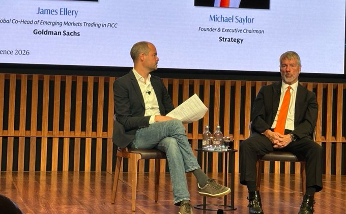Two men sit on stage at a Goldman Sachs event, with James Ellery (Global Co-Head of Emerging Markets Trading in FICC) and Michael Saylor (Founder & Executive Chairman of Strategy) identified on the backdrop. The image captures the July 2 appearance where Saylor spoke while Bitcoin was trading at $61,400, which has since risen 28%.