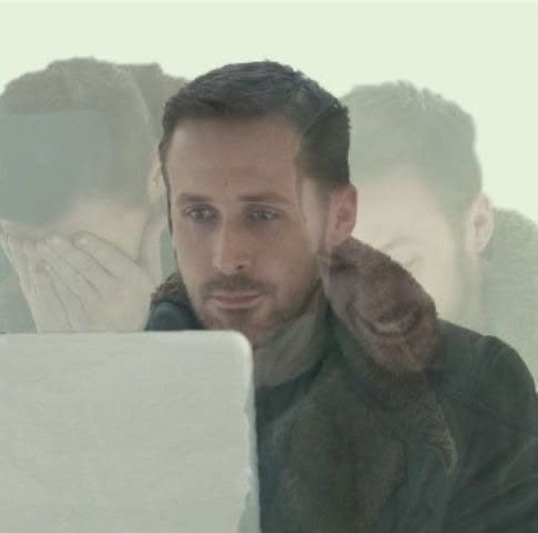 A man with short dark hair and a beard stares intently at a laptop screen with a reflection visible on the glass.