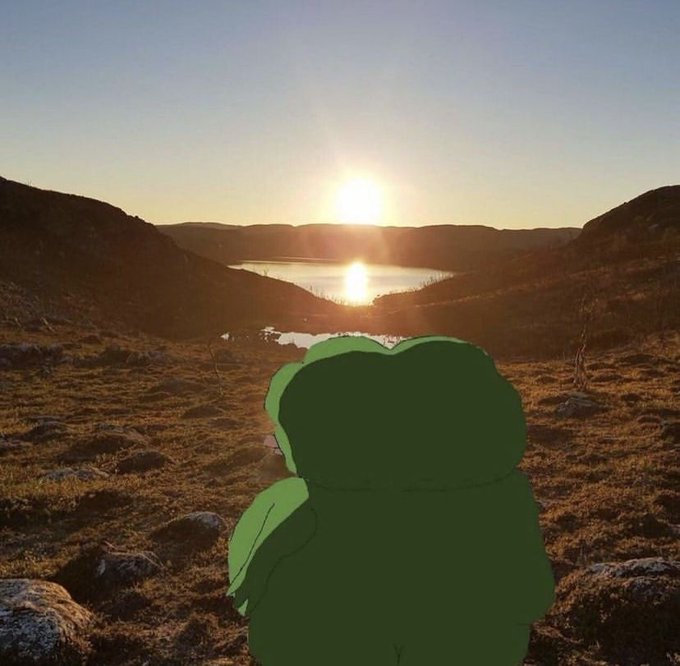 A green cartoon character sits on a mossy hilltop overlooking a lake at sunset, watching the sun dip behind distant hills.