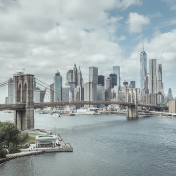 The Brooklyn Bridge spans the East River with the Lower Manhattan skyline, including One World Trade Center, visible in the background. The image connects to the post by depicting New York City, where Attorney General Letitia James and 17 other AGs are opposing the Clarity Act.