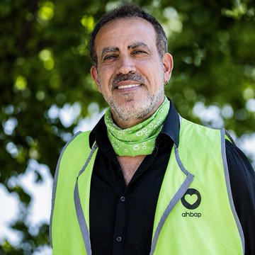 A smiling man wearing a green Ambop high-visibility vest and a green bandana around his neck, with the "ambop" logo and heart symbol visible on his vest.

The image shows a man in an Ambop safety vest, though he does not appear to be directly pictured in the accompanying text about crypto victims and betting breaches of trust.