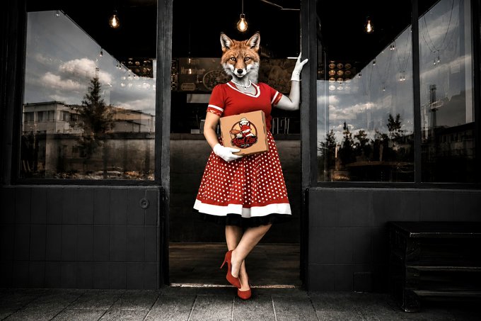 The image features a woman dressed in a red dress, holding a pizza box with a cartoon fox on it. The fox appears to be wearing a top hat and coat, giving the impression that she is a character from a story or movie. The setting of the image seems to be outdoors, as there are trees visible in the background. The post includes text such as "My deepest gratitude to these 12 incredible and top‑tier artists for collecting Cherry Merry: @TechMental_ ×5 @Papaliof_NFT ×5 @gmanxrp2 ×5 @cyberocelot29 ×2 @GummyLSD ×2 @TheTezos ×2 ...". The woman's outfit and the presence of a pizza box with a cartoon fox on it create an interesting and visually appealing scene.