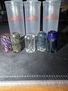 Three clear plastic "Rek Tipz" containers sit behind four colorful, swirled glass tips and a clear glass piece, displayed on a dark surface—showcasing the premium smoking accessories highlighted in the post.