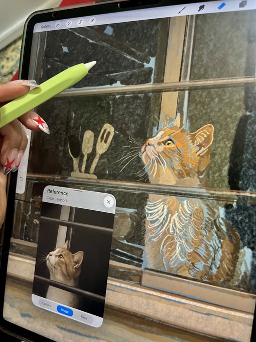 A person uses an Apple Pencil on an iPad to digitally paint a tabby cat on a window, with a reference photo of the cat visible on the screen.