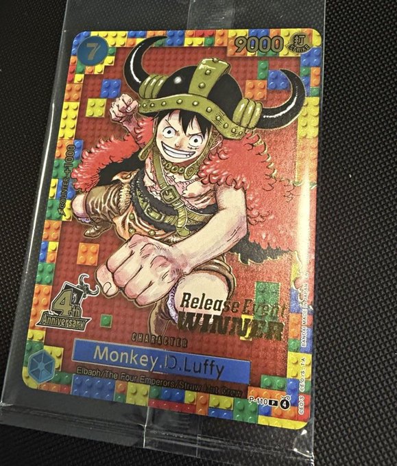 A collectible One Piece trading card featuring Monkey D. Luffy is shown in a protective sleeve, with '9000' and 'Release Fighter' text visible on the colorful block-patterned design.