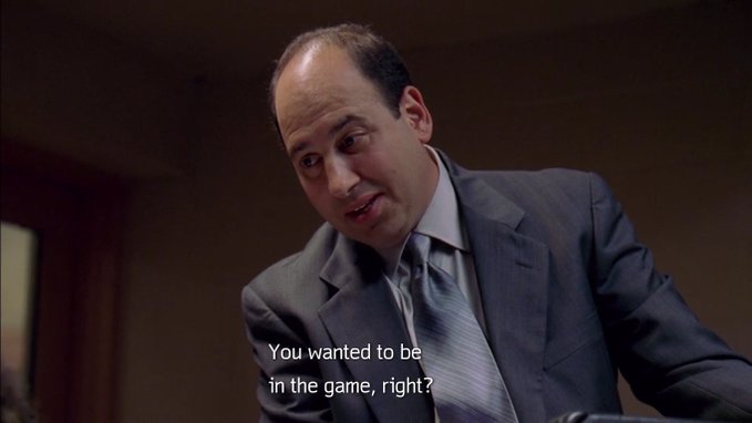 A man in a gray suit and tie with the subtitle 'You wanted to be in the game, right?' appearing at the bottom of the frame.