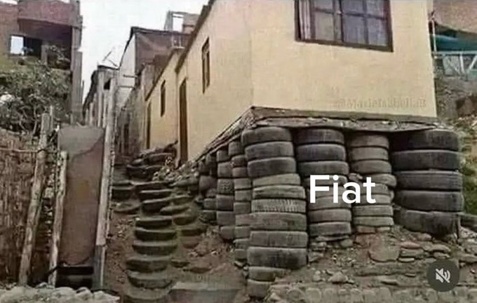 A house is precariously propped up on stacks of used tires, with the word 'Fiat' overlaid as a meme comparing the currency to an unstable foundation.