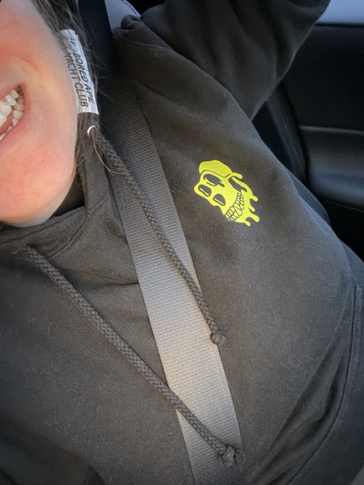 A close-up selfie shows someone smiling, wearing a dark hoodie with a bright yellow-green skull and headphones graphic, secured by a seatbelt in a car. The skull logo ties into the "Happy mutant Monday" and "Apefest" theme referenced in the post.