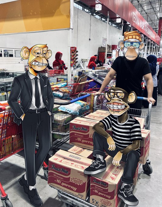 A composite image showing a real person in a hypermarket pushing a cart full of Indomie Mi Goreng boxes, with two cartoon monkey characters wearing sunglasses added in the foreground.