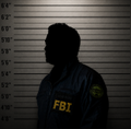 A silhouetted FBI agent stands against a height chart backdrop, wearing a jacket with "FBI" prominently displayed in yellow lettering. The image visually accompanies the news of the agent's arrest in connection with a $1,000,000 cryptocurrency theft, evoking the classic mugshot aesthetic.