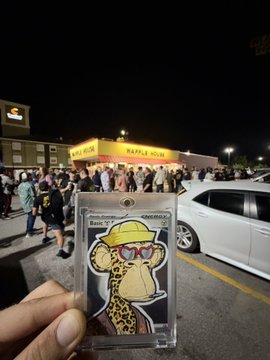 A hand holds a graded Bored Ape Yacht Club NFT card in front of a Waffle House restaurant at night.