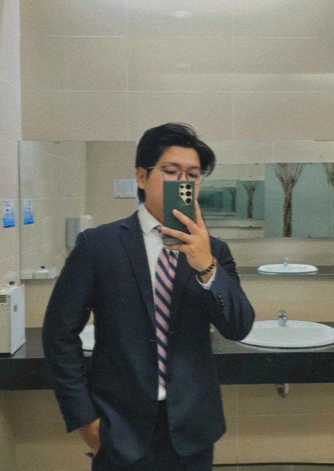 A young man in a dark suit, pink-and-navy striped tie, and glasses takes a mirror selfie with a green smartphone in a public restroom, reflecting the slightly awkward "trying to look professional" vibe of a transitional web phase. The post's "web 2.5" joke plays off his polished-but-casual look—somewhere between traditional business attire and a casual phone shot, mirroring the in-between stage of internet evolution.