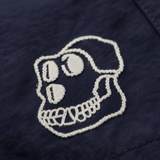 A white embroidered skull logo with a wide toothy grin stitched onto dark navy blue fabric.