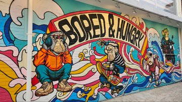 A vibrant mural on a wall featuring stylized characters including a monkey, a horse, and other figures, with bold text reading 'BORED & HUNGRY' across the top.