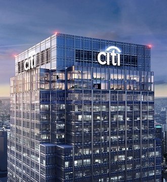 An aerial photograph of a tall office tower at dusk featuring illuminated Citi (Citigroup) signage on its glass facade.