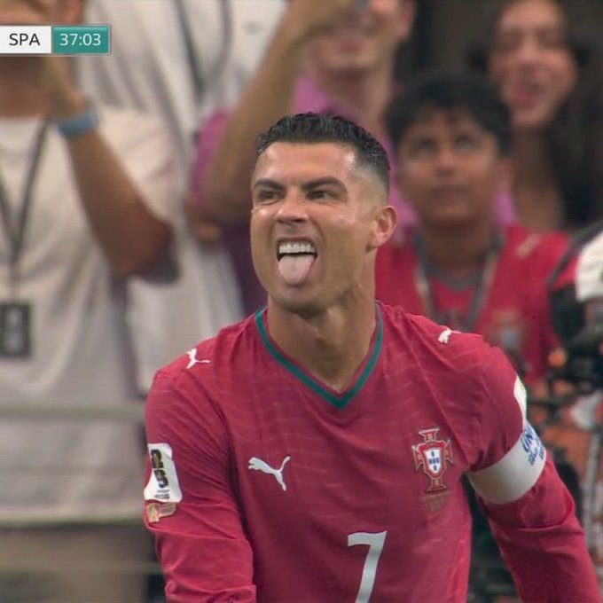Soccer player Cristiano Ronaldo, wearing a red Portugal national team jersey with the number 7, sticks out his tongue during a match, with the score 'SPA 37:03' visible in the top left corner.