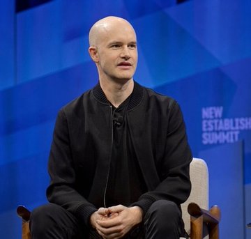 A bald man in a black jacket sits on a stage with his hands clasped, speaking at the 'NEW ESTABLISH SUMMIT'.