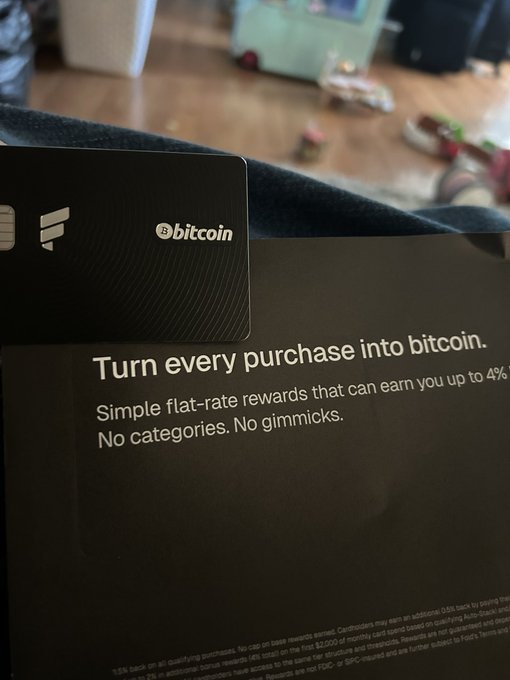 The image shows a black envelope with a white Bitcoin card inside, which has text that reads "Turn every purchase into Bitcoin" along with some other information about Bitcoins. The envelope appears to be addressed to someone named "Bob".