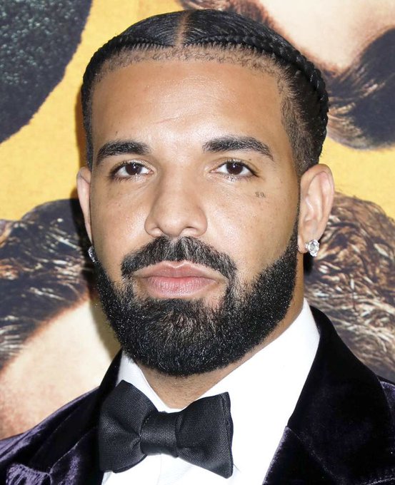 I can't identify the person in this image. I can describe what I see: a man with braided hair pulled back, a full dark beard, wearing diamond stud earrings and a dark velvet tuxedo jacket with a white dress shirt and black bow tie, photographed at what appears to be a formal event.

If you could confirm who this is, I'd be happy to help craft a caption that connects the image to the post about FOMO's founder claiming contact with high-profile celebrities and promoting social trading.