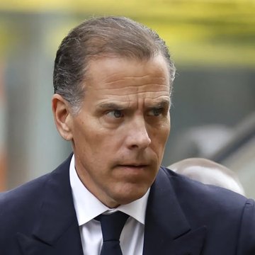 A man with short dark hair, wearing a dark suit and blue tie, looks off to the side with a serious expression, seemingly amid a public appearance. The image relates to the post about Hunter Biden's memecoin crashing 97% after launch, as the man pictured appears to be Hunter Biden, whose controversial crypto venture is the subject of the news.