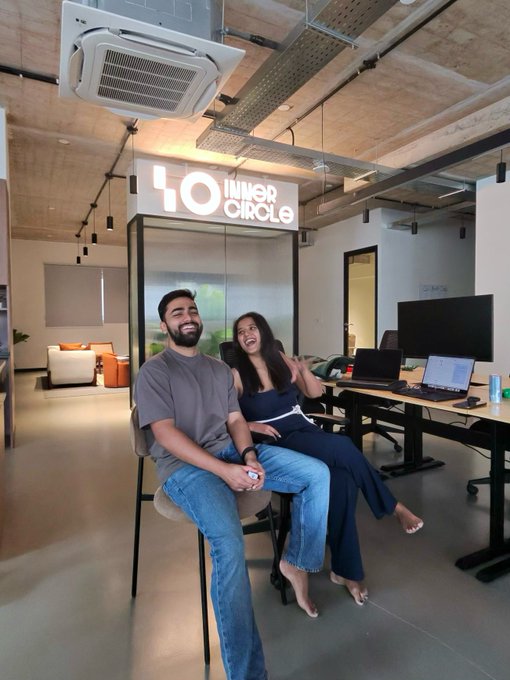 A man and a woman sitting together and smiling in a modern office space under a sign that reads 'INNER CIRCLE'.