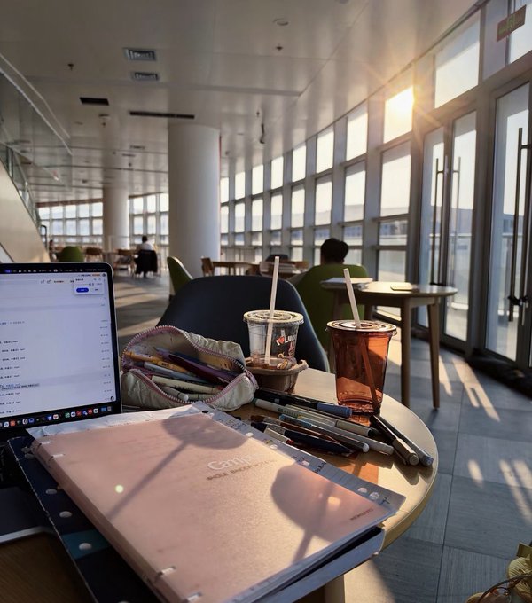 A study session at a sunlit café features an open "GOJU Real Leather" binder, scattered pens, an iced tea, and a laptop, reflecting the post's theme of learning trading techniques through diligent note-taking and research.