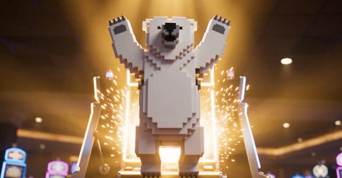 A large LEGO polar bear sculpture stands triumphantly with raised arms on a stage illuminated by dramatic golden lights and confetti, suggesting a grand reveal or celebration event.
