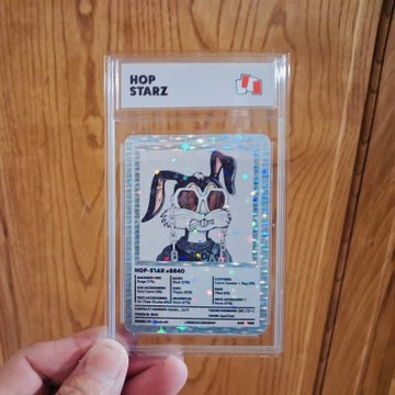 A hand holding a graded 'HOP STARZ' trading card featuring a colorful illustration of a rabbit character wearing sunglasses, encased in a protective plastic slab.