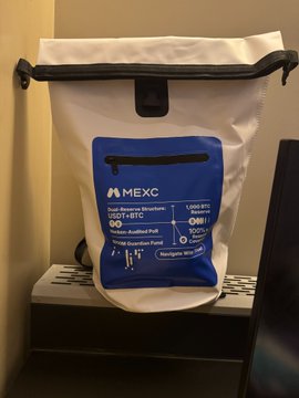 A white MEXC branded dry bag/backpack displayed on a shelf, featuring product specifications including Dual Storage Structure, -20°C to +50°C temperature range, and USB-C/Navigator WPC compatibility.