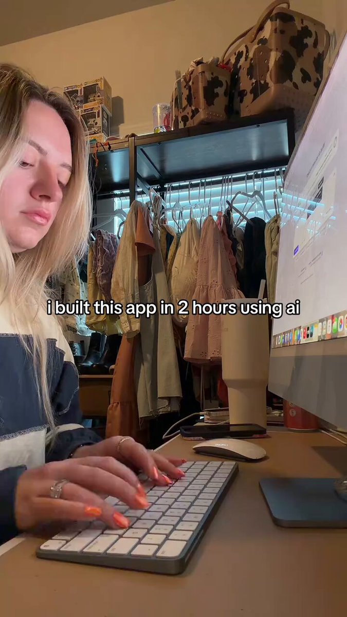 The image shows a woman sitting at a desk with a computer monitor, keyboard, mouse, and cup of coffee. She appears to be working or browsing the internet while wearing a blue and white striped shirt. The photo also contains text that reads "I built this app in 2 hours using AI". This suggests that the woman has created an application for herself, possibly related to her work or personal interests.