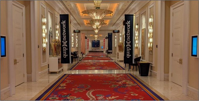 The image shows an elegant hotel conference hallway with red patterned carpets, ornate chandeliers, and "QUIP Network" banners, along with Toshiba signage in the background. The setting reflects the post's message about QUIP Network's role in advancing quantum-resistant security and decentralized infrastructure.