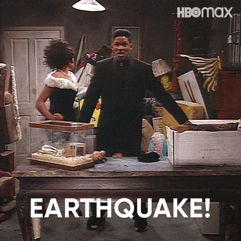 The image features a man standing at a table with a box of items, including a TV and some other objects. The text "Earthquake!" is written above him, indicating that there has been an earthquake recently or could be one soon.