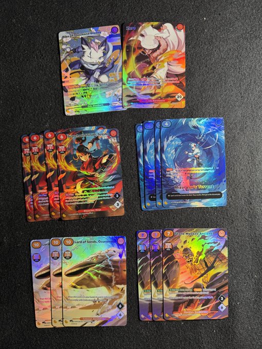 A collection of holographic Azuki NFT trading cards arranged on a dark surface, with multiple duplicates of cards like "Kurogane Wagi (Orange)" and "Lord of Sands, Osamurais" visible alongside other unique alt cards. The image illustrates the post's sentiment about receiving multiple duplicate copies ("dupes") of alternate art cards from Azuki boxes.