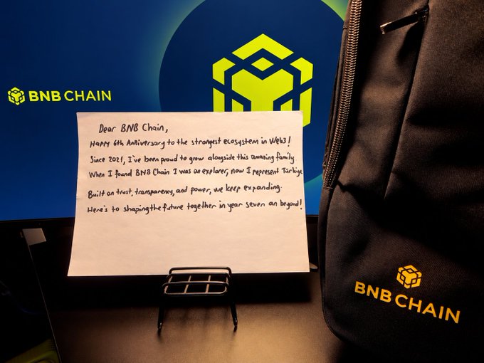 A handwritten letter on a stand celebrates BNB Chain's 6th anniversary, addressing the "strongest ecosystem in Web3," alongside a branded backpack bearing the BNB Chain logo, reflecting the author's pride in representing Türkiye since joining the community in 2021.