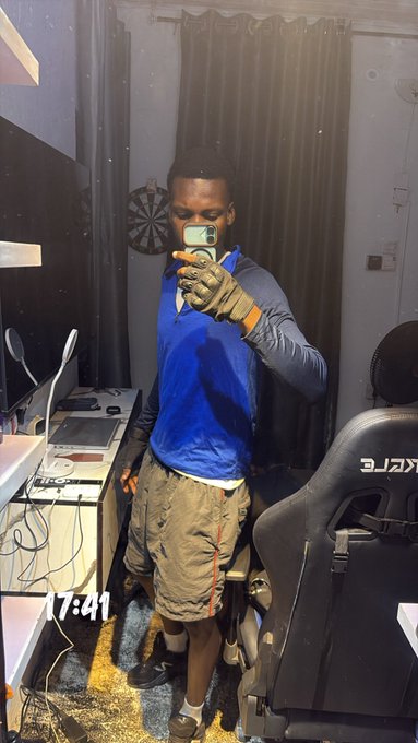 A man in a blue hoodie, khaki shorts, and a tactical glove takes a mirror selfie in a gaming room at 17:41.