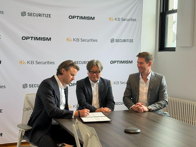 Three men in business attire sit at a table during a signing ceremony, with a backdrop displaying logos for 'SECURITIZE', 'OPTIMISM', and 'KB Securities'.