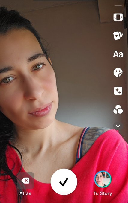 A selfie screenshot on Snapchat showing a woman in a red top with the Spanish interface option "Atrás" and "Tu Story" visible.