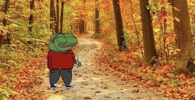 A cartoon frog character wearing a red sweater and blue pants stands on a dirt path surrounded by autumn foliage in a forest.