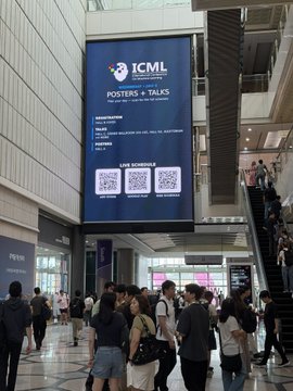 A photo of a shopping mall with an 'ICML Posters + Talks' banner displaying a schedule and QR codes, with a crowd of people walking below.