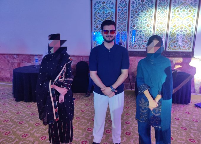 Three people pose together at the MEXC Pakistan Musical Dinner Night event, with the central figure wearing sunglasses and a dark polo shirt flanked by two individuals in traditional shalwar kameez attire, set against an ornately decorated backdrop featuring intricate Islamic-style patterns and ambient purple lighting.