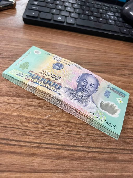 A thick stack of Vietnamese 500,000 Dong banknotes resting on a wooden desk next to a black computer keyboard.