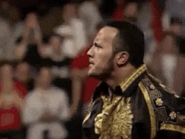 The image features a man wearing a gold and black outfit, possibly a suit or a costume, with a gold and black jacket that has a floral pattern. The man appears to be looking off into the distance, suggesting he might be at an event or gathering where people are watching him. In the background, there is a crowd of people who seem to be engaged in conversation or observing something happening on stage. The image also contains text that reads "Smells like $ALGO". This could possibly be related to the event taking place, as it might be a themed party or a special occasion where attendees are encouraged to wear costumes and participate in various activities.