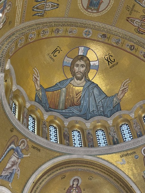 An interior view of an ornate golden dome featuring a mosaic of Jesus Christ Pantocrator with the Greek inscriptions 'IC' and 'XC', surrounded by religious figures and mosaic arches.