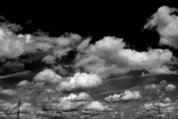 A dramatic black and white photograph captures billowing cumulus clouds scattered across a dark sky, with the silhouettes of electrical transmission towers visible along the bottom horizon, perfectly complementing the "In the Clouds" and "Clearness" titles from the accompanying post.