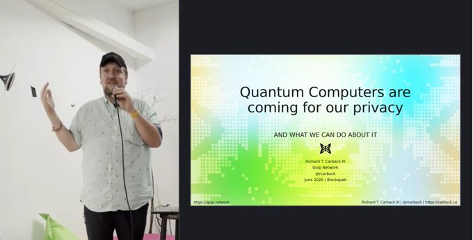 A man in a cap and patterned shirt speaks into a microphone during a presentation titled 'Quantum Computers are coming for our privacy AND WHAT WE CAN DO ABOUT IT' by Richard T. Carback III.