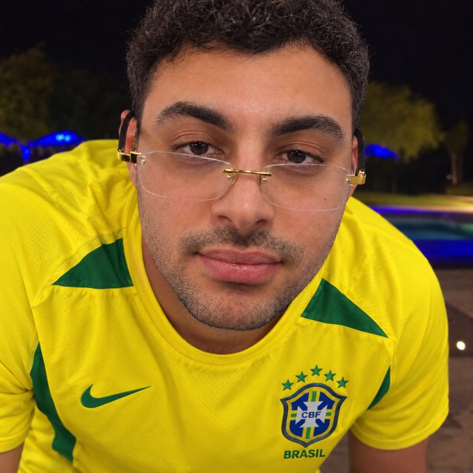 A man poses wearing the iconic yellow Brazil national football jersey featuring the "CBF BRASIL" crest and Nike swoosh, playfully leaning into the post's joke about being a "Brazilian guy." Rimless glasses and a nighttime outdoor setting complete the casual selfie-style portrait.