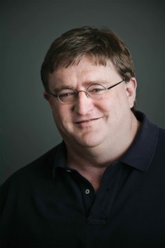 A portrait of a smiling man with glasses wearing a dark blue polo shirt against a gray background.