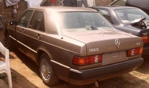 A gold/tan Mercedes-Benz 190E sedan parked outdoors with clothes hanging on a line visible in the background.