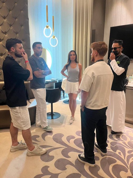A casually dressed group of five people gather in a stylishly decorated lounge with modern pendant lighting and patterned floors, sharing a relaxed conversation. The "GM" (good morning) caption suggests the image captures a friendly morning meet-up among the group.