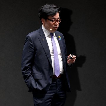 In this image, there's a person dressed in a suit and tie standing next to a wall with black background. The man appears to be an actor or speaker, as he has a microphone attached to his suit. It seems like he may be giving a presentation or speech at a conference or event. In the image description provided, it is referred to as "BIG: Tom Lee says Bitmine's Ethereum treasury generates $1M per day in staking rewards." This text suggests that the man might be discussing cryptocurrency or blockchain technology and how it affects the financial world.